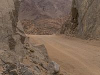 a small vehicle traveling across a barren road between some large rocks and boulders on one side