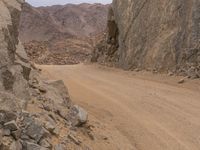 a small vehicle traveling across a barren road between some large rocks and boulders on one side