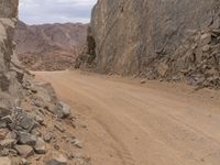 a small vehicle traveling across a barren road between some large rocks and boulders on one side