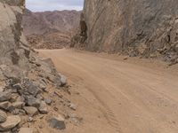 a small vehicle traveling across a barren road between some large rocks and boulders on one side