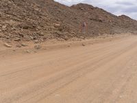 a small vehicle traveling across a barren road between some large rocks and boulders on one side