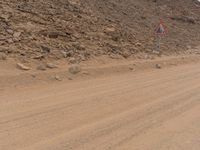 a small vehicle traveling across a barren road between some large rocks and boulders on one side