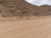 a small vehicle traveling across a barren road between some large rocks and boulders on one side