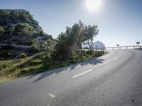 the road is winding on the side of a mountain with trees around it and the ocean in the distance