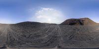 a large pile of sand and dirt with clouds in the background on the beach under a blue sky