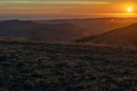 a person that is sitting on a hill with some horses by a sunset on a clear day