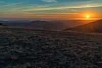 a person that is sitting on a hill with some horses by a sunset on a clear day