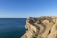 an empty cliff and a body of water in the distance on a clear day, as viewed from a sea stack