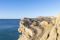 an empty cliff and a body of water in the distance on a clear day, as viewed from a sea stack