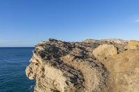 an empty cliff and a body of water in the distance on a clear day, as viewed from a sea stack