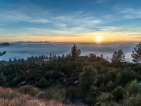 sun setting over the hills and the valleys below the clouds at dusk, above a layer of fog