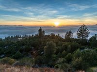 sun setting over the hills and the valleys below the clouds at dusk, above a layer of fog