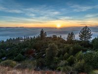 sun setting over the hills and the valleys below the clouds at dusk, above a layer of fog