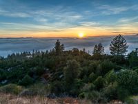 sun setting over the hills and the valleys below the clouds at dusk, above a layer of fog