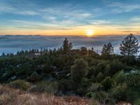 sun setting over the hills and the valleys below the clouds at dusk, above a layer of fog