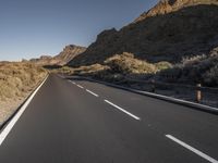 the road is empty of traffic in the desert area of the mountains below them, there is a person on the bike