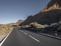 the road is empty of traffic in the desert area of the mountains below them, there is a person on the bike