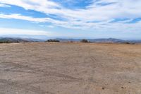 a lone motorcycle in an open desert field with the sky in the background with a couple of clouds above