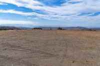 a lone motorcycle in an open desert field with the sky in the background with a couple of clouds above