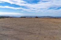 a lone motorcycle in an open desert field with the sky in the background with a couple of clouds above