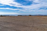 a lone motorcycle in an open desert field with the sky in the background with a couple of clouds above