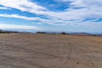 a lone motorcycle in an open desert field with the sky in the background with a couple of clouds above