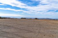 a lone motorcycle in an open desert field with the sky in the background with a couple of clouds above