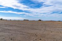 a lone motorcycle in an open desert field with the sky in the background with a couple of clouds above