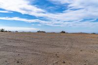 a lone motorcycle in an open desert field with the sky in the background with a couple of clouds above