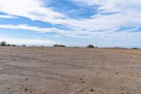 a lone motorcycle in an open desert field with the sky in the background with a couple of clouds above