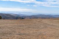 the view of some hills in the distance from above a barren field with a person on a bicycle on the side of it