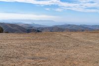 the view of some hills in the distance from above a barren field with a person on a bicycle on the side of it