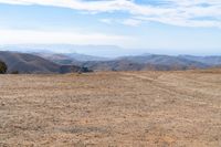 the view of some hills in the distance from above a barren field with a person on a bicycle on the side of it