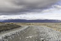 an empty road surrounded by barren mountains and bushes under a cloudy sky, as if in nature