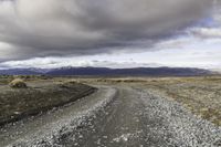 an empty road surrounded by barren mountains and bushes under a cloudy sky, as if in nature