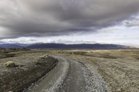 an empty road surrounded by barren mountains and bushes under a cloudy sky, as if in nature