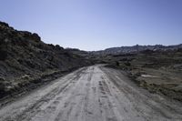 gravel road in the desert near mountains with rocks and bushes on either side of the dirt road