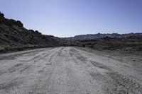 gravel road in the desert near mountains with rocks and bushes on either side of the dirt road