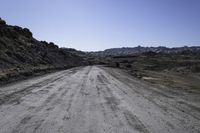 gravel road in the desert near mountains with rocks and bushes on either side of the dirt road