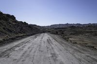 gravel road in the desert near mountains with rocks and bushes on either side of the dirt road