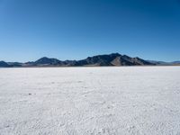 a large desert plain with several mountains on one side and the sky blue sky in the background