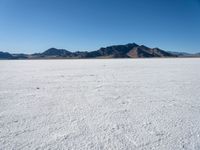 a large desert plain with several mountains on one side and the sky blue sky in the background