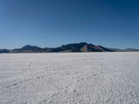 a large desert plain with several mountains on one side and the sky blue sky in the background