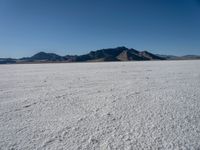 a large desert plain with several mountains on one side and the sky blue sky in the background