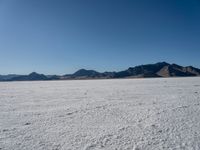 a large desert plain with several mountains on one side and the sky blue sky in the background