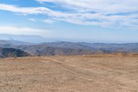 a dog is on a dirt hill while looking at the mountains from atop a mountain