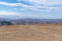 a dog is on a dirt hill while looking at the mountains from atop a mountain