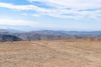 a dog is on a dirt hill while looking at the mountains from atop a mountain