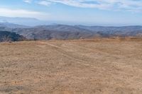 a dog is on a dirt hill while looking at the mountains from atop a mountain