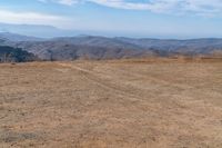 a dog is on a dirt hill while looking at the mountains from atop a mountain